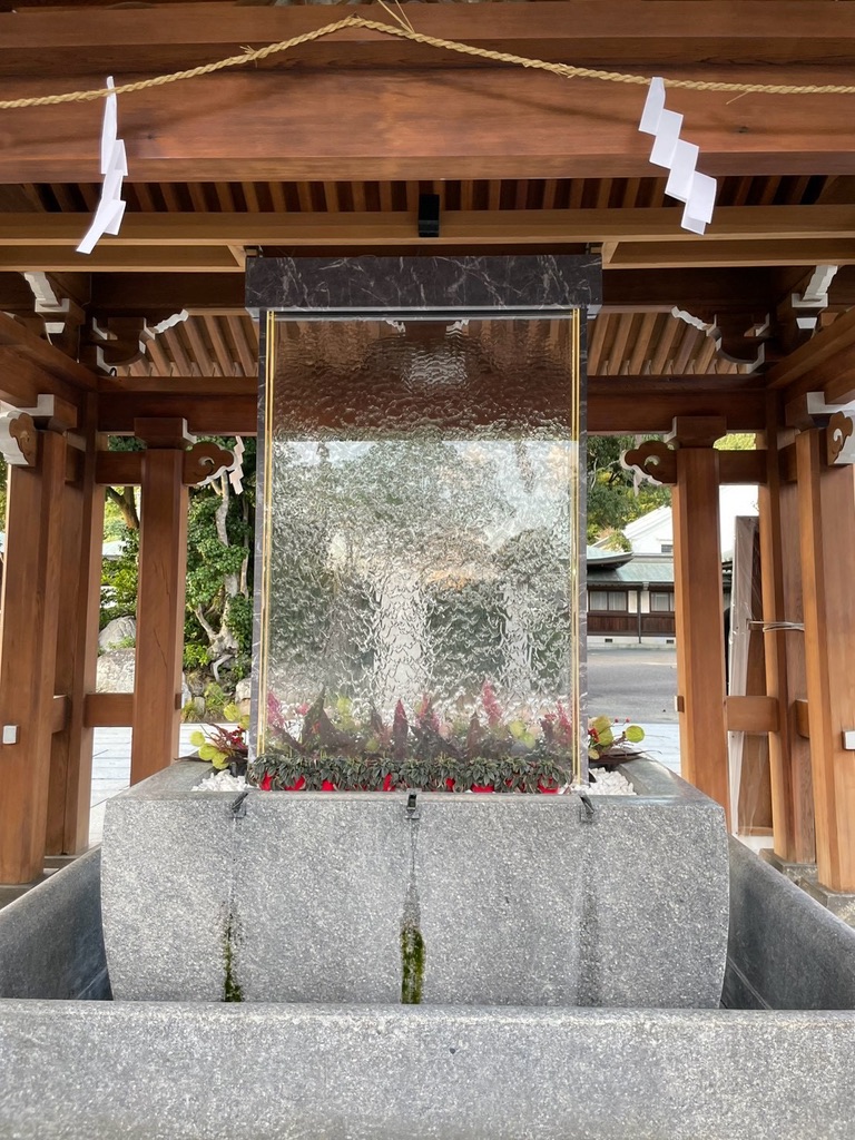 宮地嶽神社の手水舎。ガラスを流れ落ちる水の壁と、足元を彩る花々