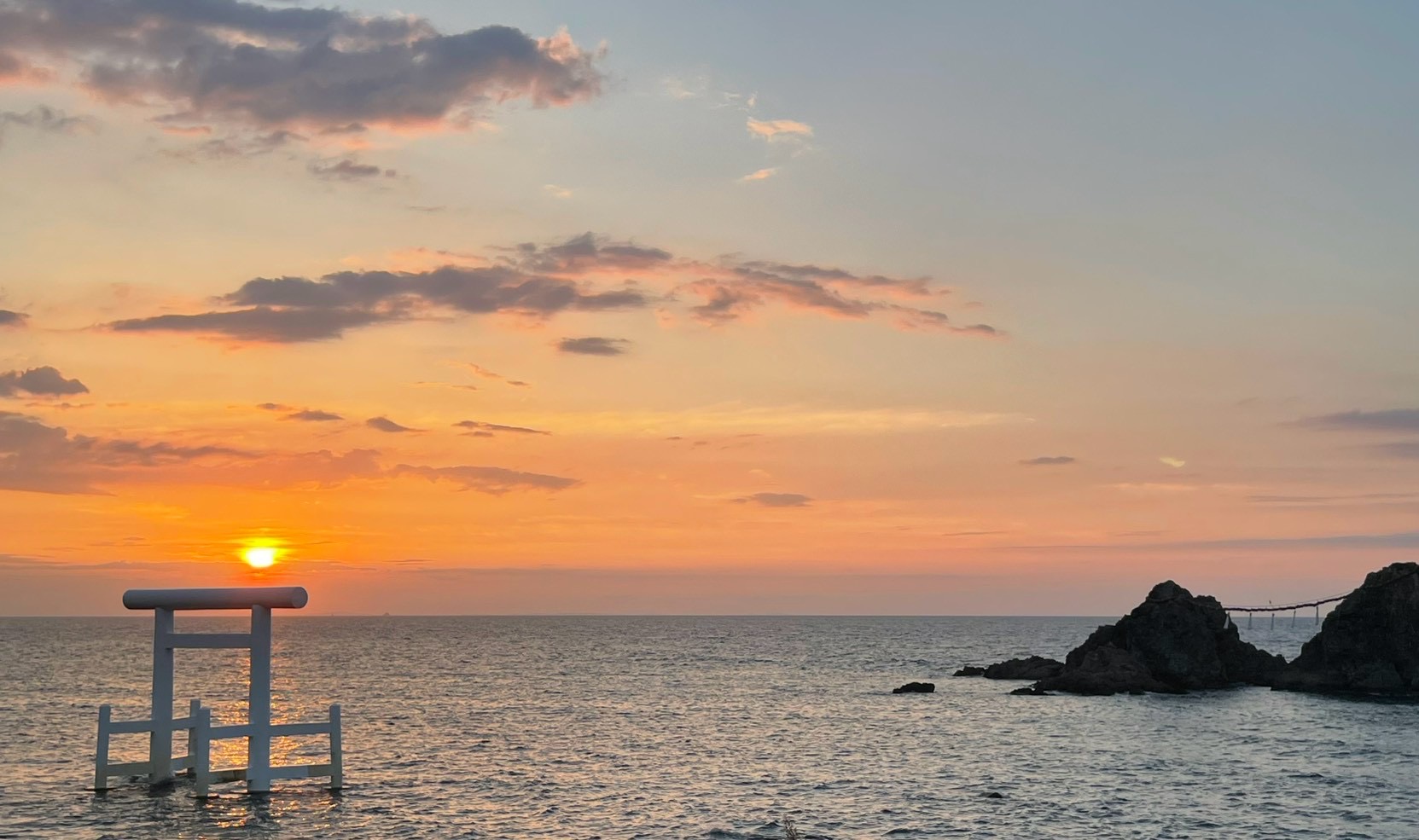 茜色に染まった桜井二見ヶ浦の夕景。潮が満ちた海に立つ白い鳥居と、右手に大注連縄で結ばれた夫婦岩