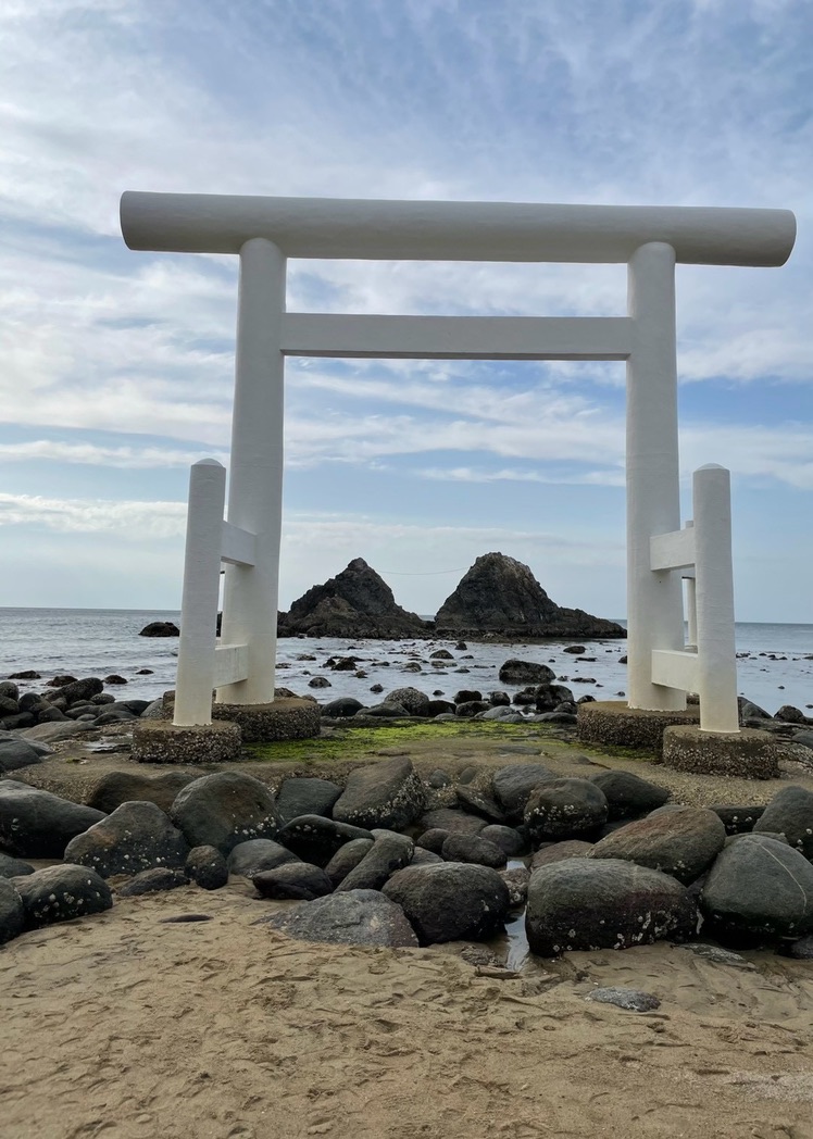 桜井二見ヶ浦の砂浜に立つ白い鳥居と、その向こうの海に浮かぶ夫婦岩